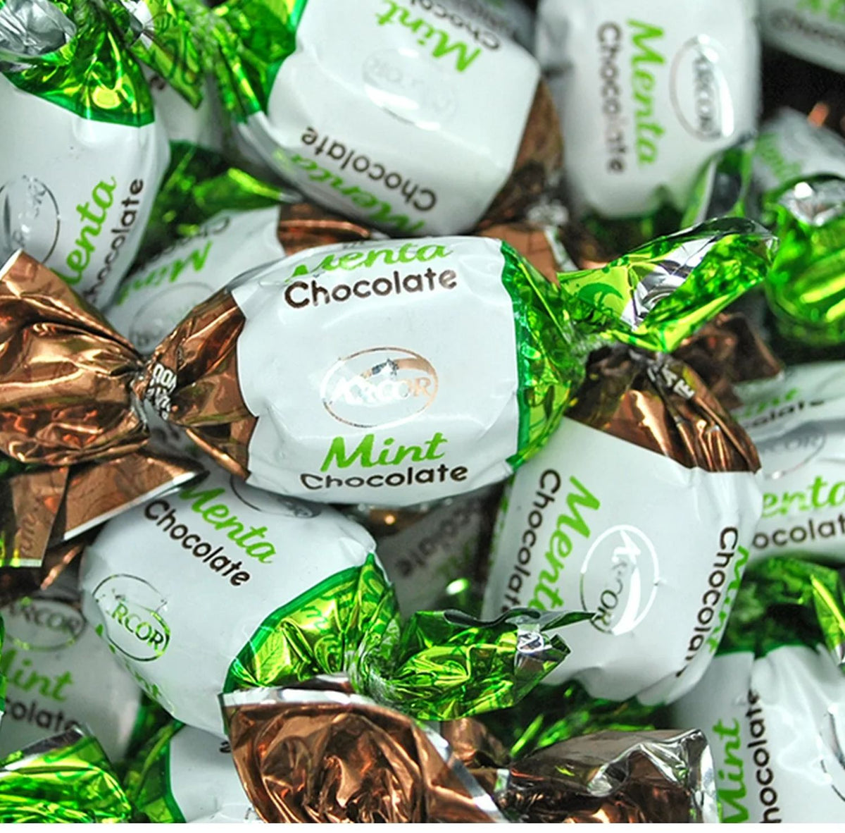 A close-up pile of wrapped chocolates labeled 'Menta Chocolate' with white paper labels and shiny green and metallic copper foil wrappers.