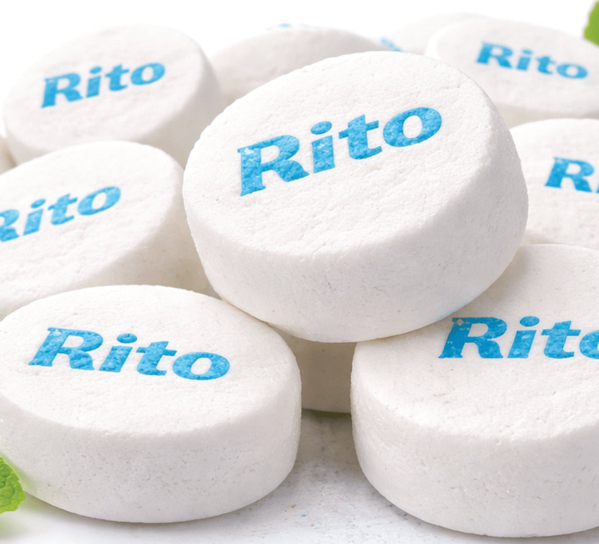 A pile of white oval Rito brand tablets with blue text, photographed close-up on a light background.